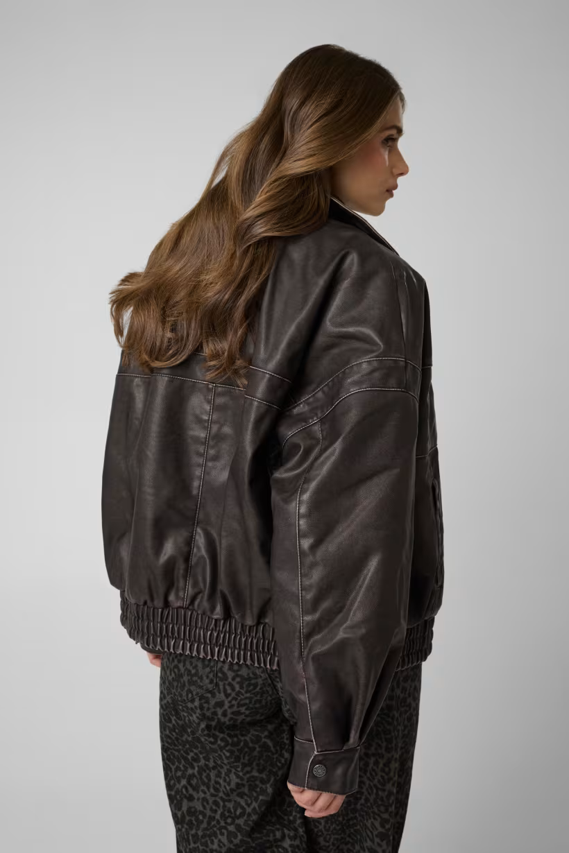 Giacca bomber Follower SRL in similpelle marrone con cuciture a contrasto indossata da una modella di spalle