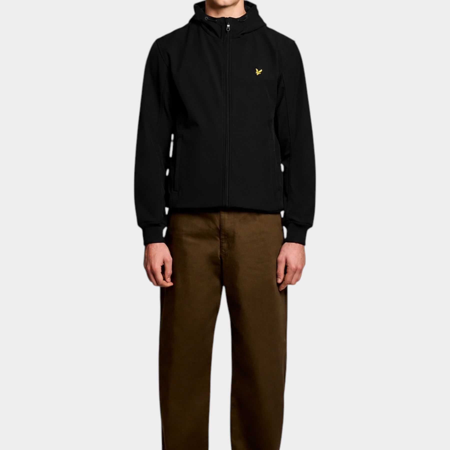 Giacca softshell nera LYLE & SCOTT con cappuccio e logo giallo, indossata da un modello con pantaloni marroni