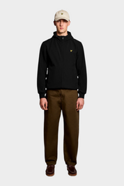 Giacca softshell nera LYLE & SCOTT con cappuccio e logo giallo, indossata da un modello con pantaloni marroni