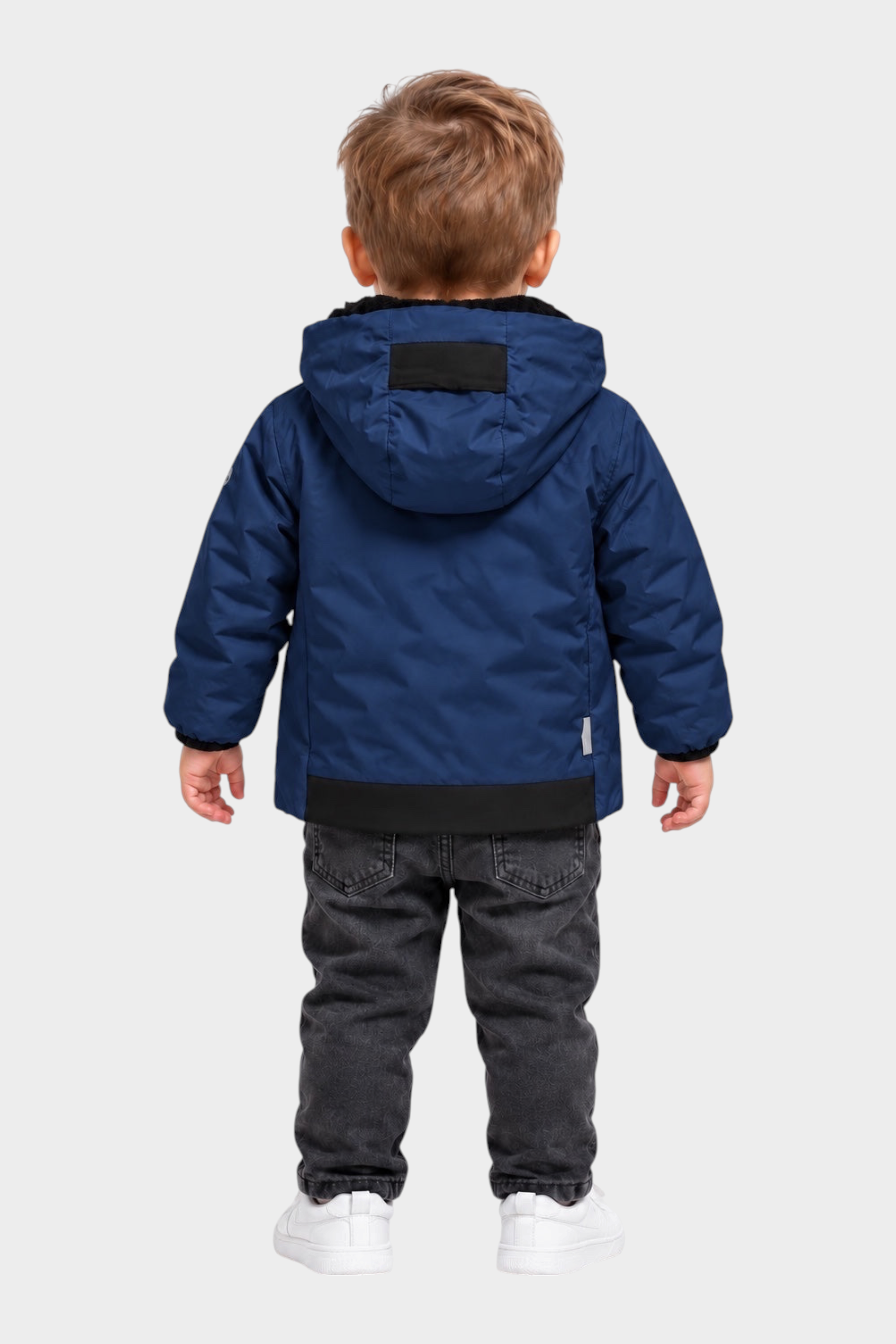 Bambino di spalle indossa un giubbino blu SUNS BOARDS in velour con cappuccio, jeans grigi e scarpe bianche