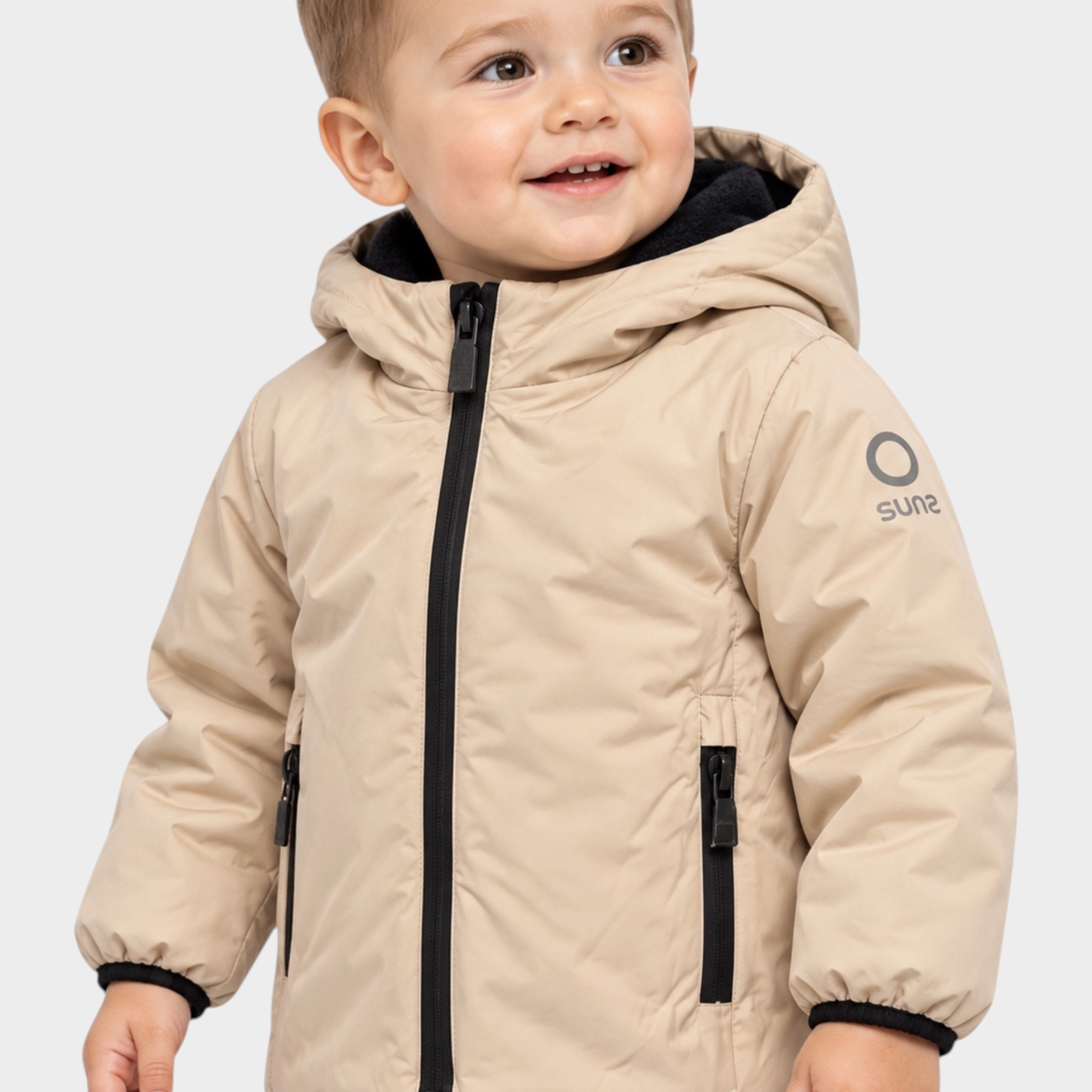 Bambino che indossa un giubbino beige Follower SRL con cappuccio, zip nera e logo SUNS BOARDS sulla manica