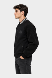 Modello indossa giubbino bomber nero Follower SRL con maniche in tessuto teddy e chiusura a bottoni a pressione