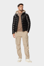 Modello indossa giubbino nero lucido con cappuccio Follower SRL, abbinato a maglia beige e pantaloni cargo