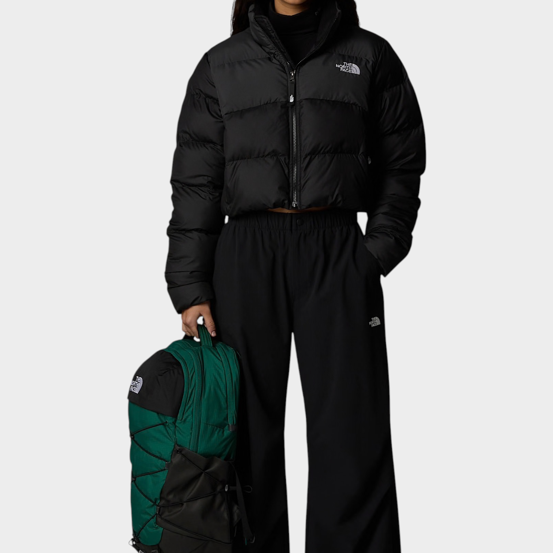 Modella indossa giubbino nero cropped Saikuru di Follower SRL con zaino verde e pantaloni neri