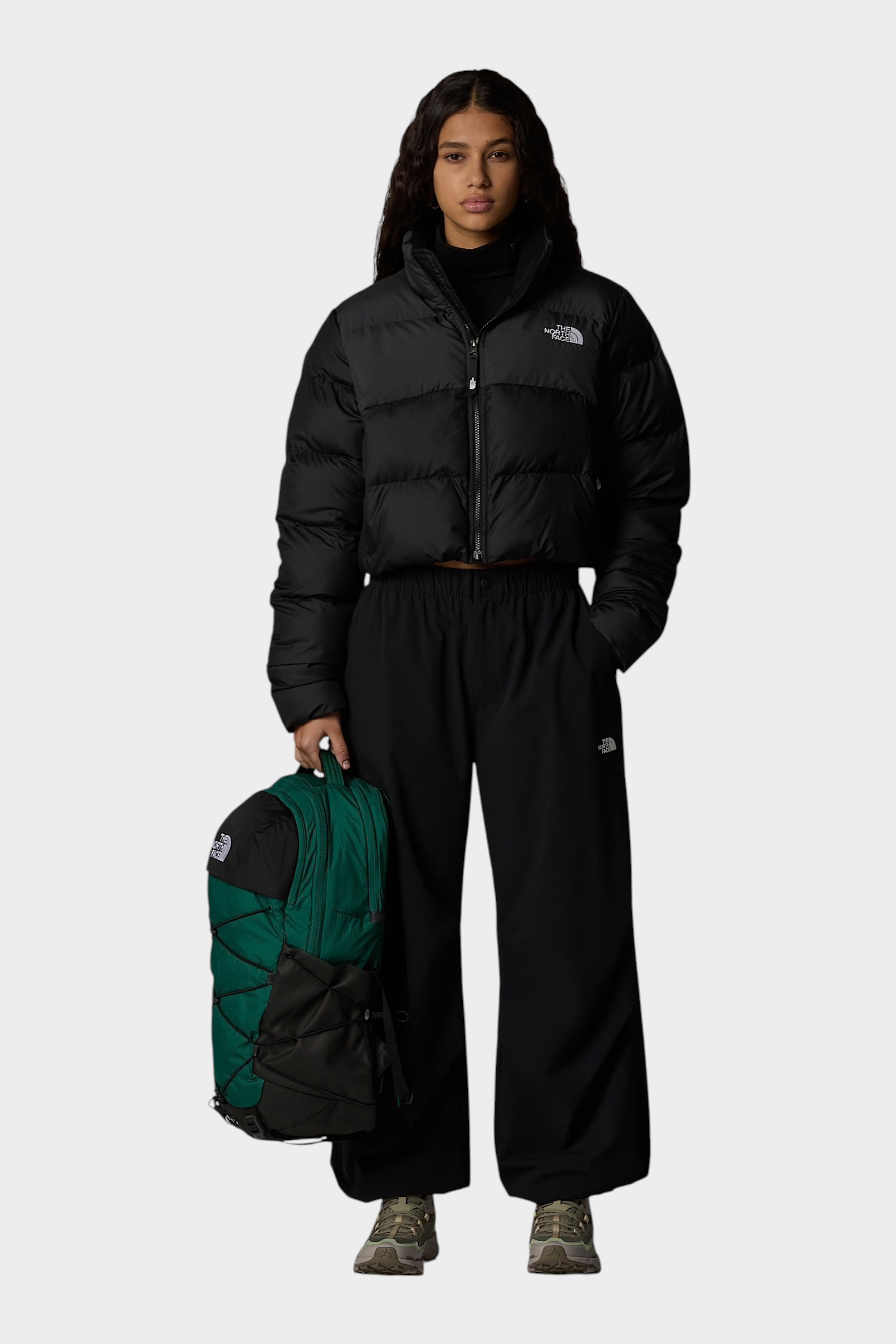 Modella indossa giubbino nero cropped Saikuru di Follower SRL con zaino verde e pantaloni neri