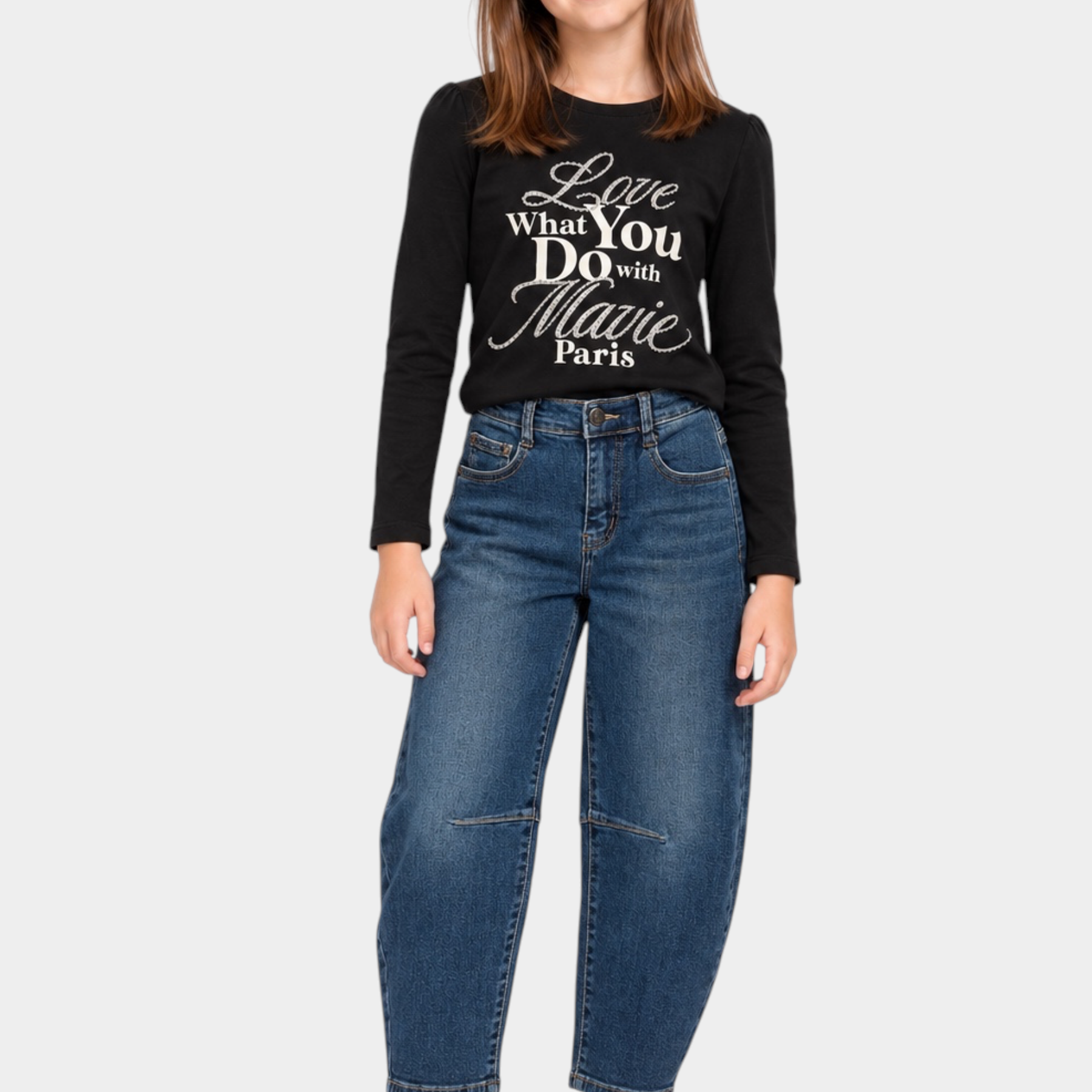 Bambina indossa jeans baggy blu Ma Vie Paris con maglia nera a maniche lunghe e sneakers bianche su sfondo bianco
