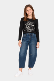 Bambina indossa jeans baggy blu Ma Vie Paris con maglia nera a maniche lunghe e sneakers bianche su sfondo bianco