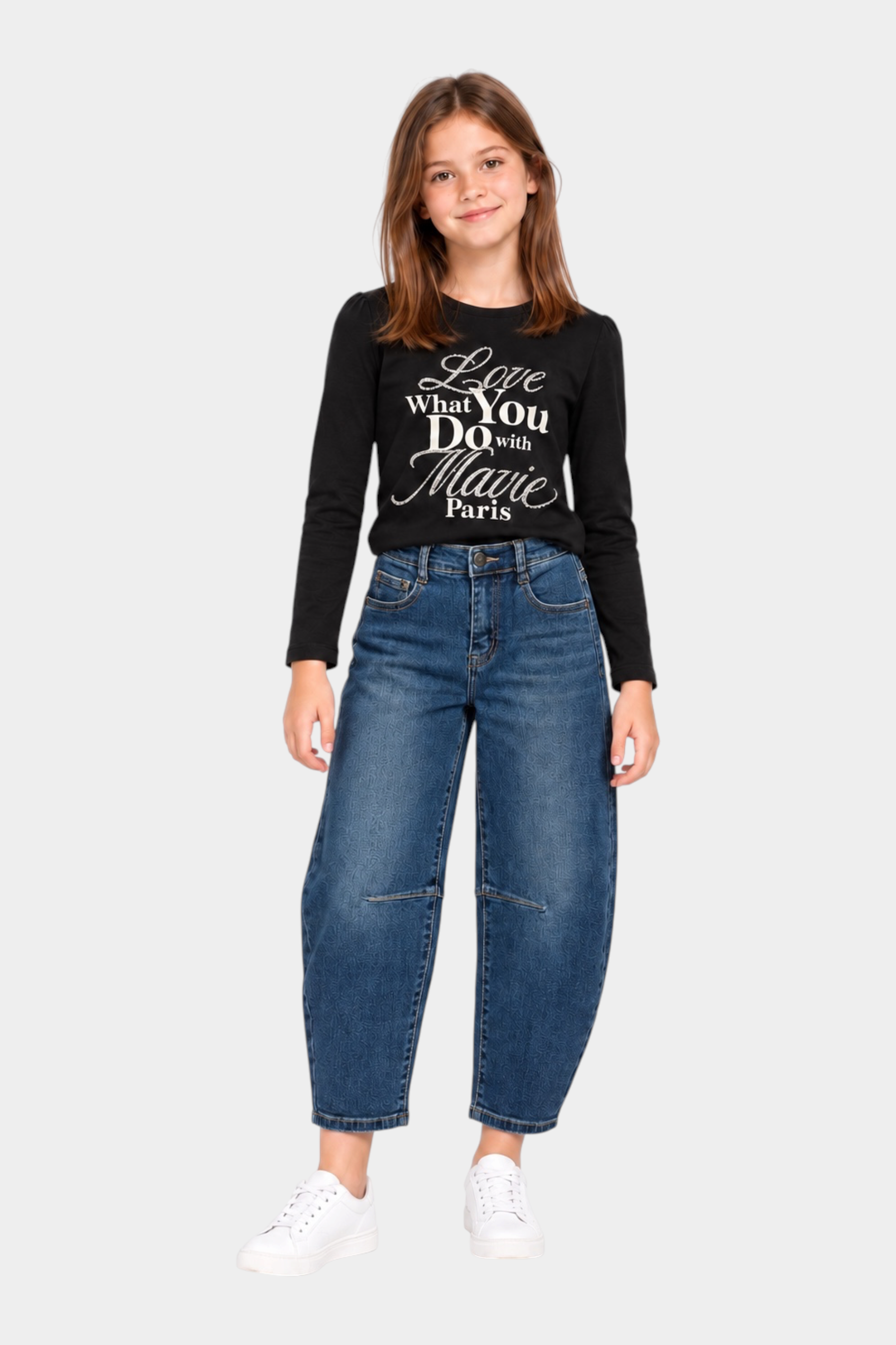 Bambina che indossa jeans baggy blu Follower SRL con maglia nera a maniche lunghe e scarpe da ginnastica bianche