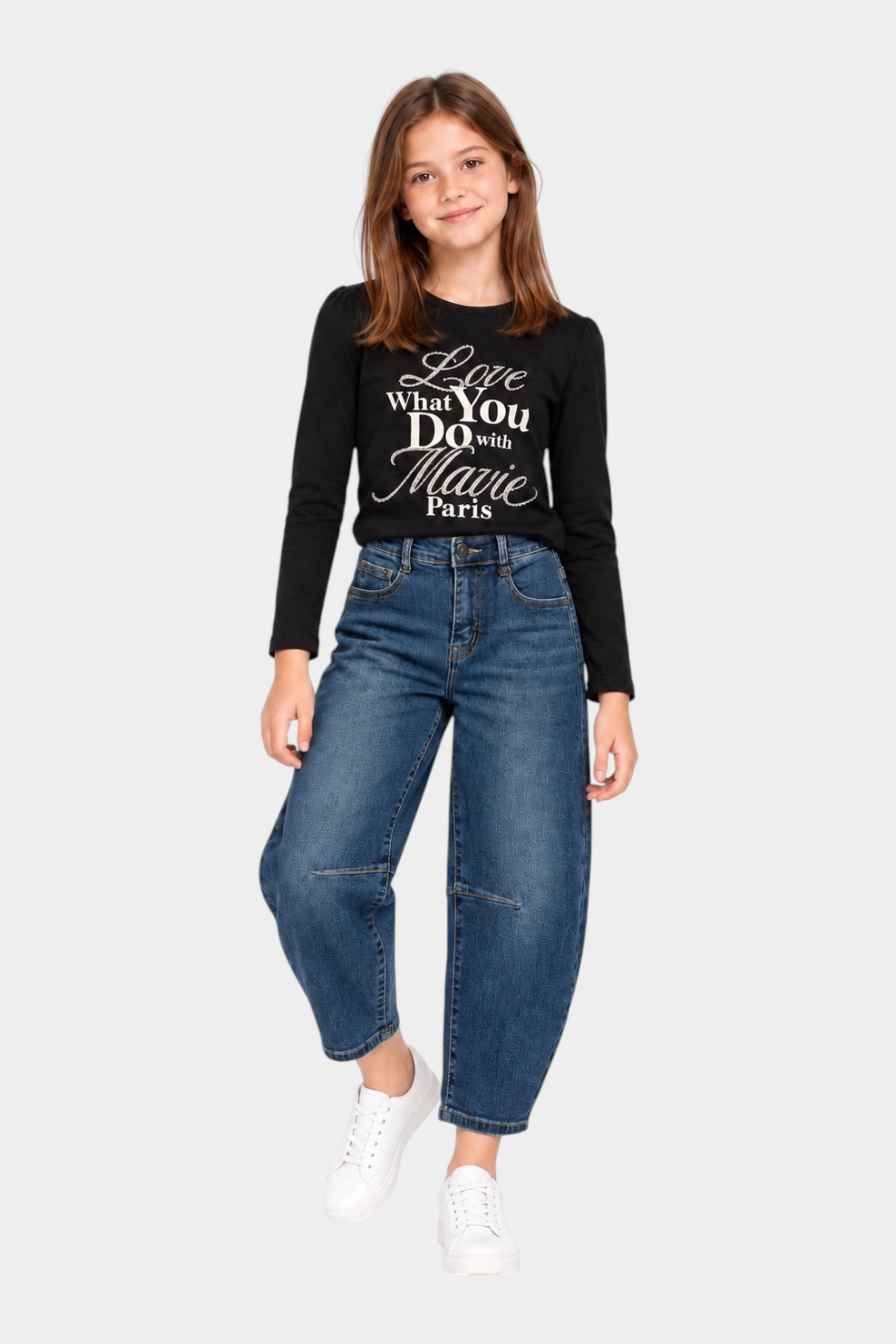Ragazza indossa jeans baggy blu Follower SRL con maglia nera a maniche lunghe e sneakers bianche su sfondo bianco