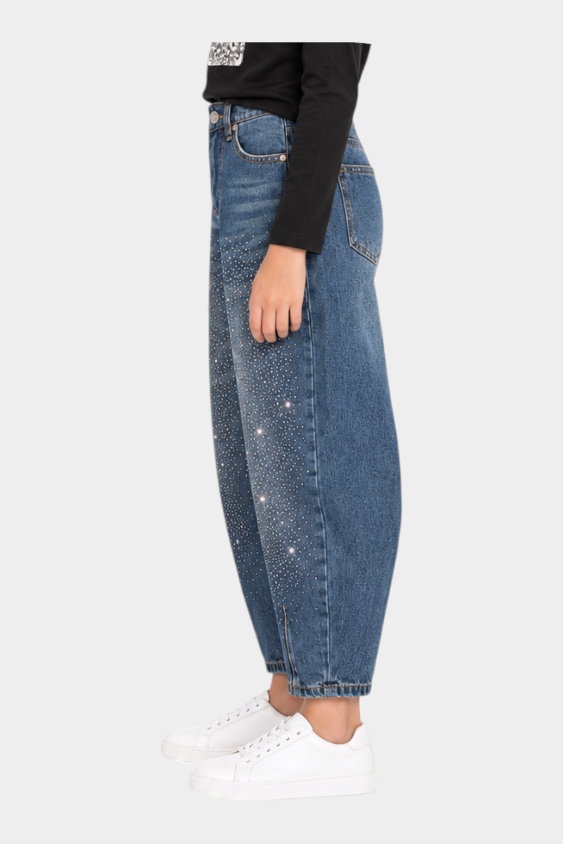 Bambina indossa jeans baggy blu con strass di Follower SRL, abbinati a maglia nera e sneakers bianche