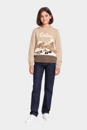 Ragazza indossa maglia girocollo beige Follower SRL con intarsio paesaggio montano Cortina e jeans scuri