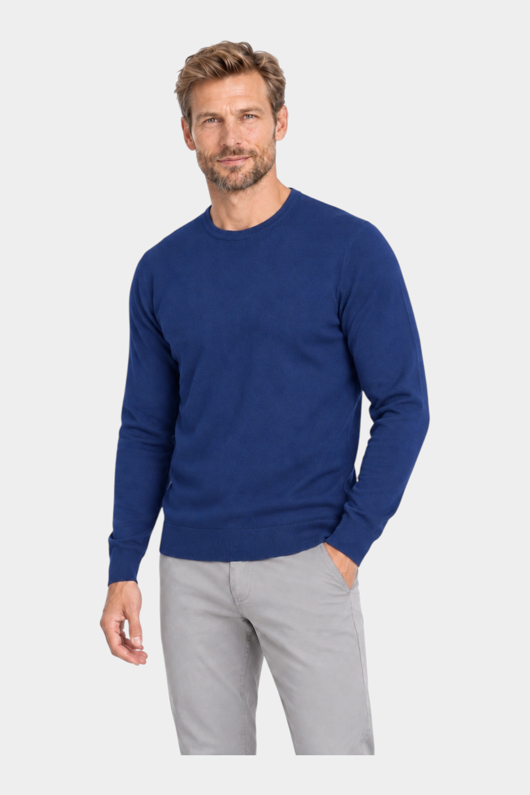 Modello indossa maglia girocollo blu in filo Ragno proposta da Follower SRL con pantaloni grigi su sfondo bianco