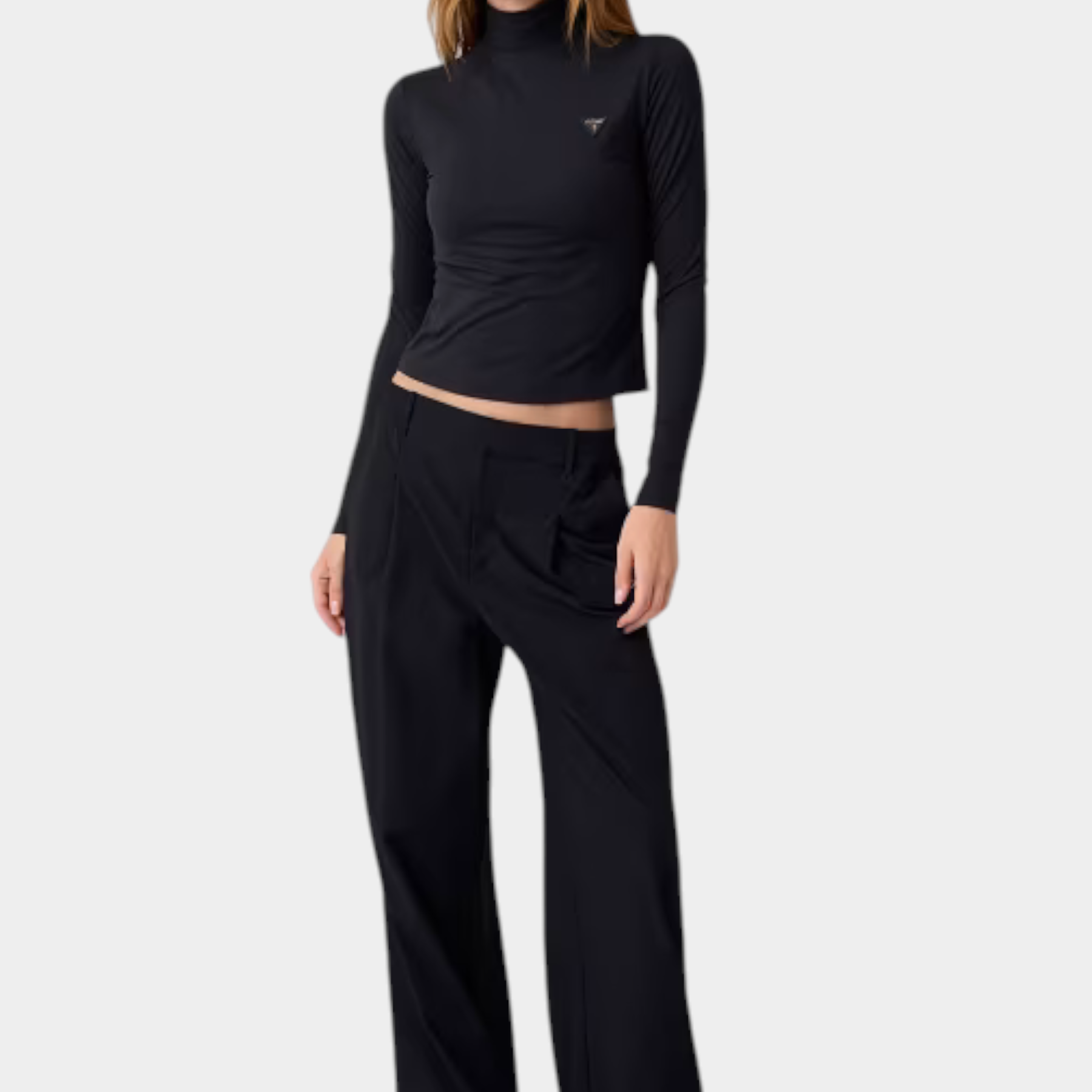 Modella indossa maglia lupetto nera in microfibra GUESS con logo metallico sul petto e pantaloni neri a gamba larga
