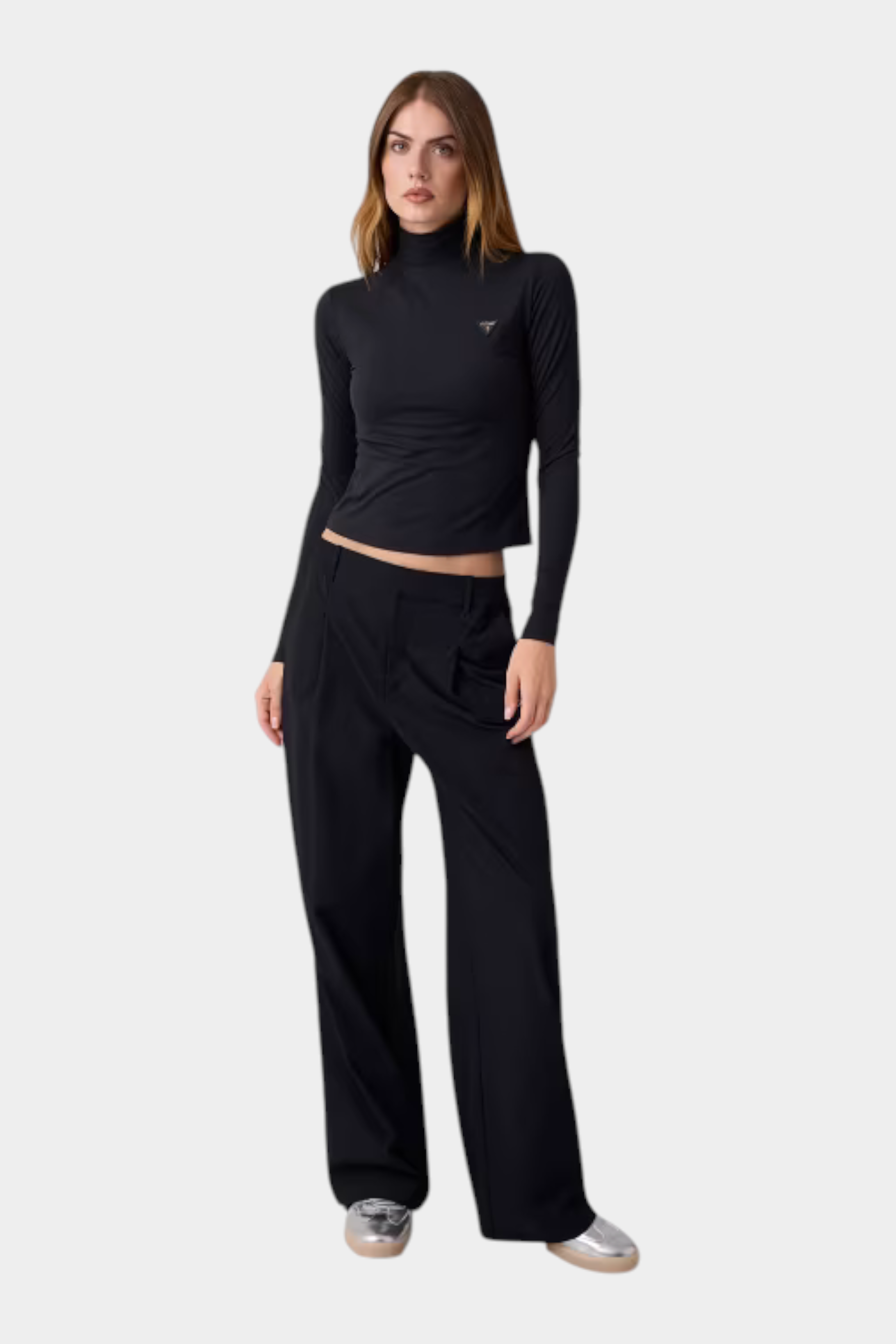 Modella indossa maglia lupetto nera in microfibra GUESS con logo metallico sul petto e pantaloni neri a gamba larga