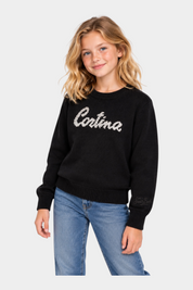 Bambina indossa maglia girocollo nera Follower SRL con scritta Cortina ricamata, maniche lunghe e polsini a costine