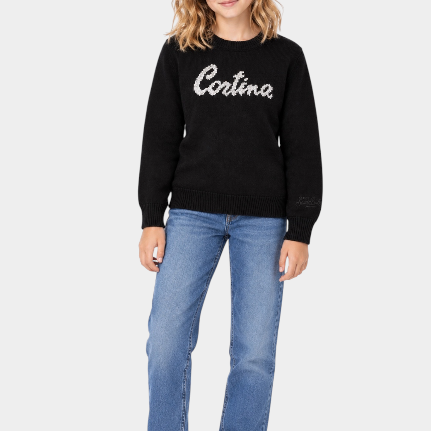 Ragazza indossa maglia girocollo nera Follower SRL con scritta Cortina in strass, abbinata a jeans e sneakers bianche