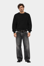 Modello indossa maglione girocollo nero a maglia larga Follower SRL con jeans grigi dal taglio ampio