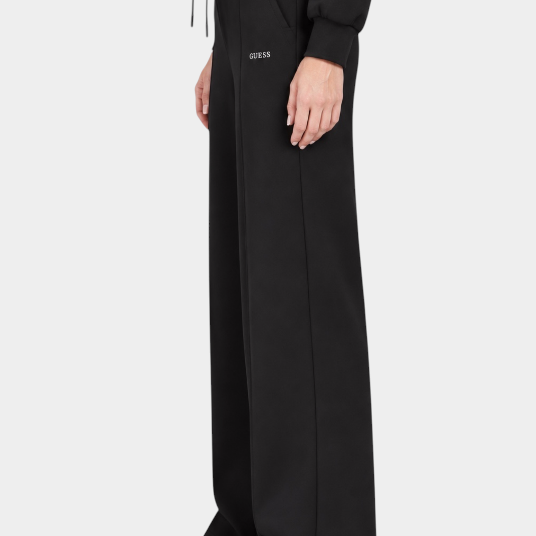 Pantalone jogger nero Follower SRL a gamba larga con logo GUESS, vista laterale su modella con sneakers bianche
