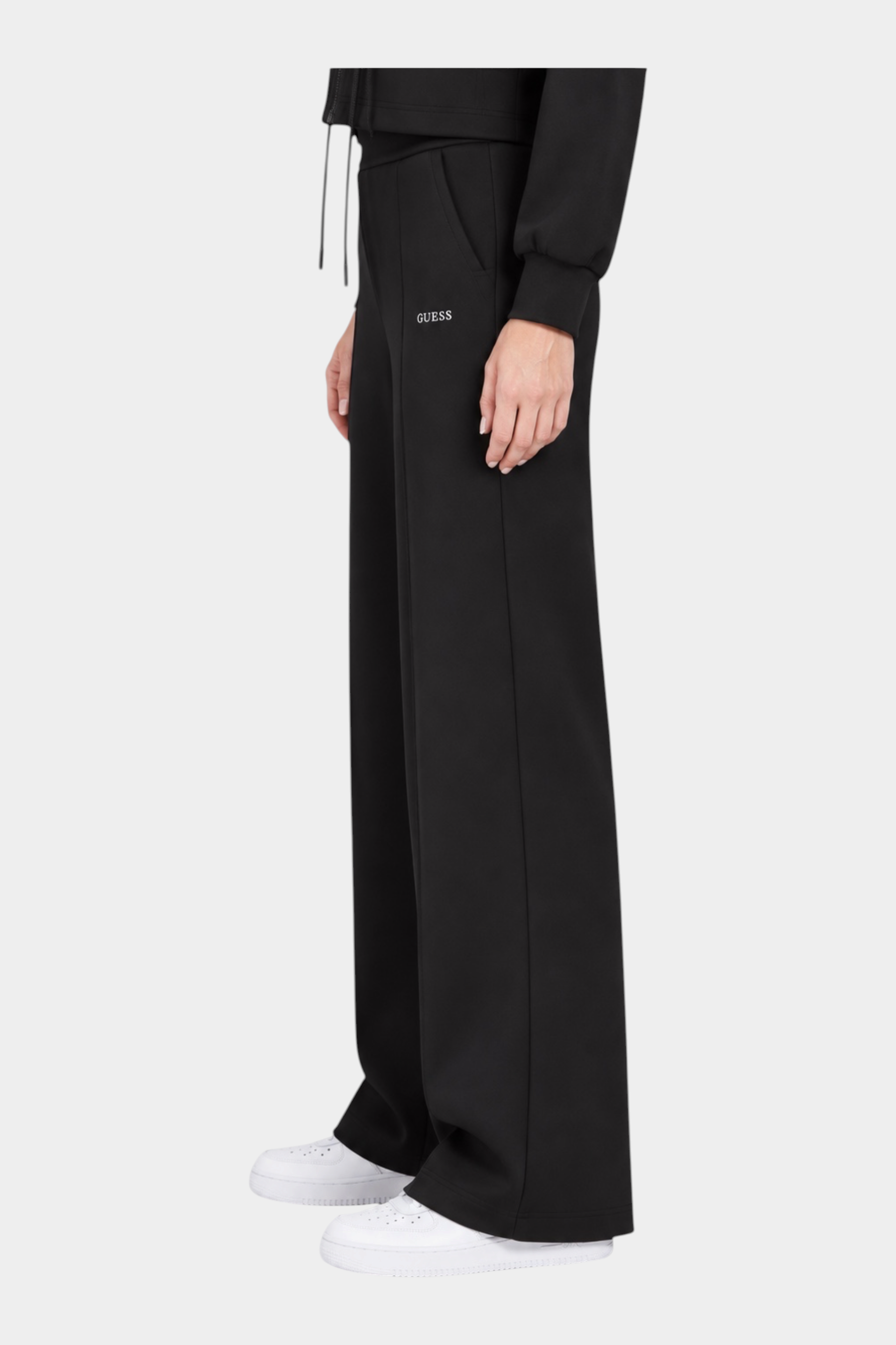 Pantalone jogger nero Follower SRL a gamba larga con logo GUESS, vista laterale su modella con sneakers bianche