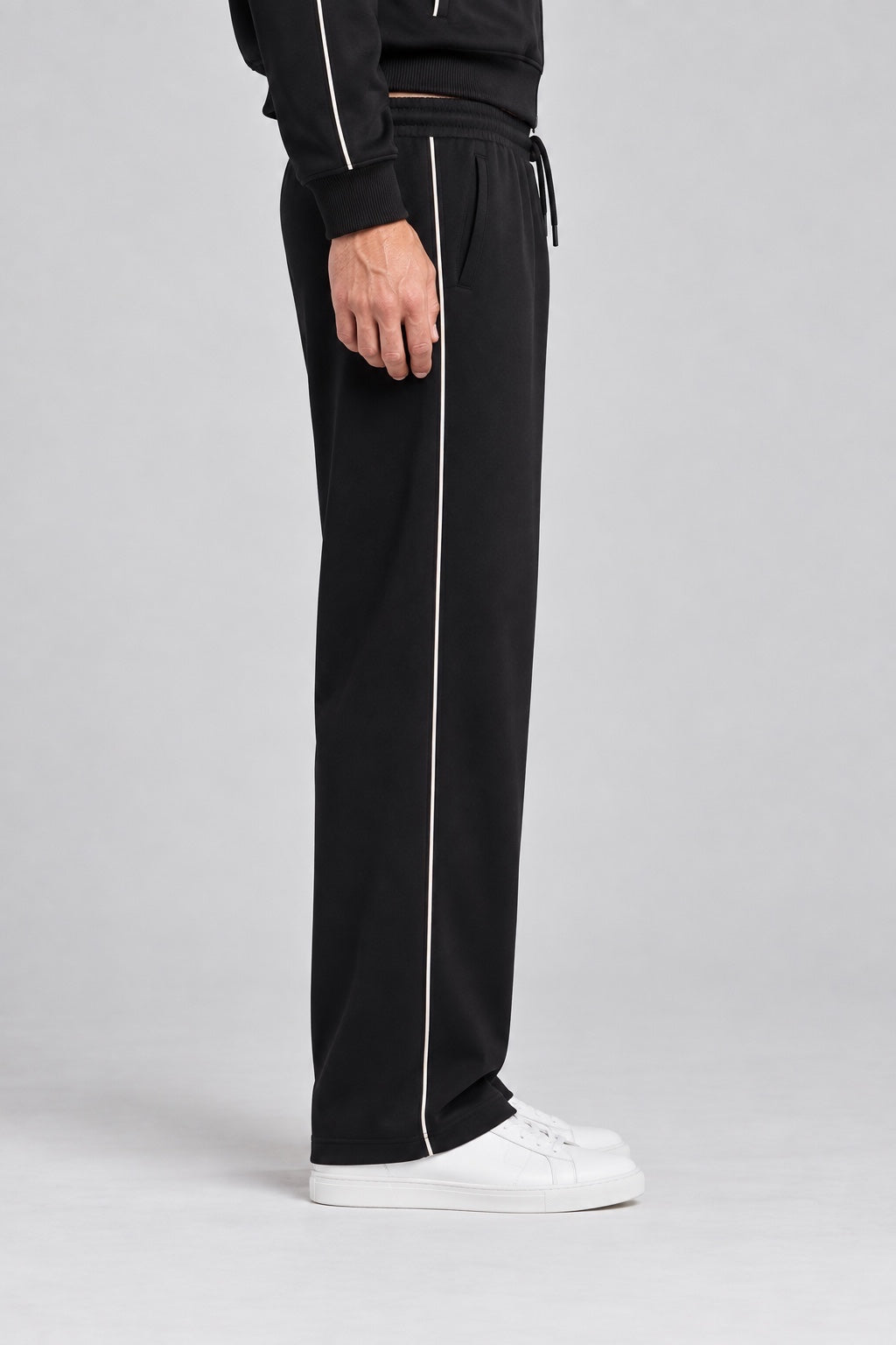 Pantalone jogger nero da uomo GUESS con riga laterale bianca, indossato con scarpe da ginnastica bianche Follower SRL