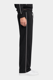 Pantalone jogger nero da uomo GUESS con riga laterale bianca, indossato con scarpe da ginnastica bianche Follower SRL
