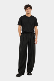 Modello indossa pantaloni baggy-fit neri con pinces di Follower SRL abbinati a una t-shirt nera e scarpe chunky