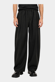 Modello indossa pantaloni baggy-fit neri con pinces di Follower SRL abbinati a una t-shirt nera su sfondo bianco