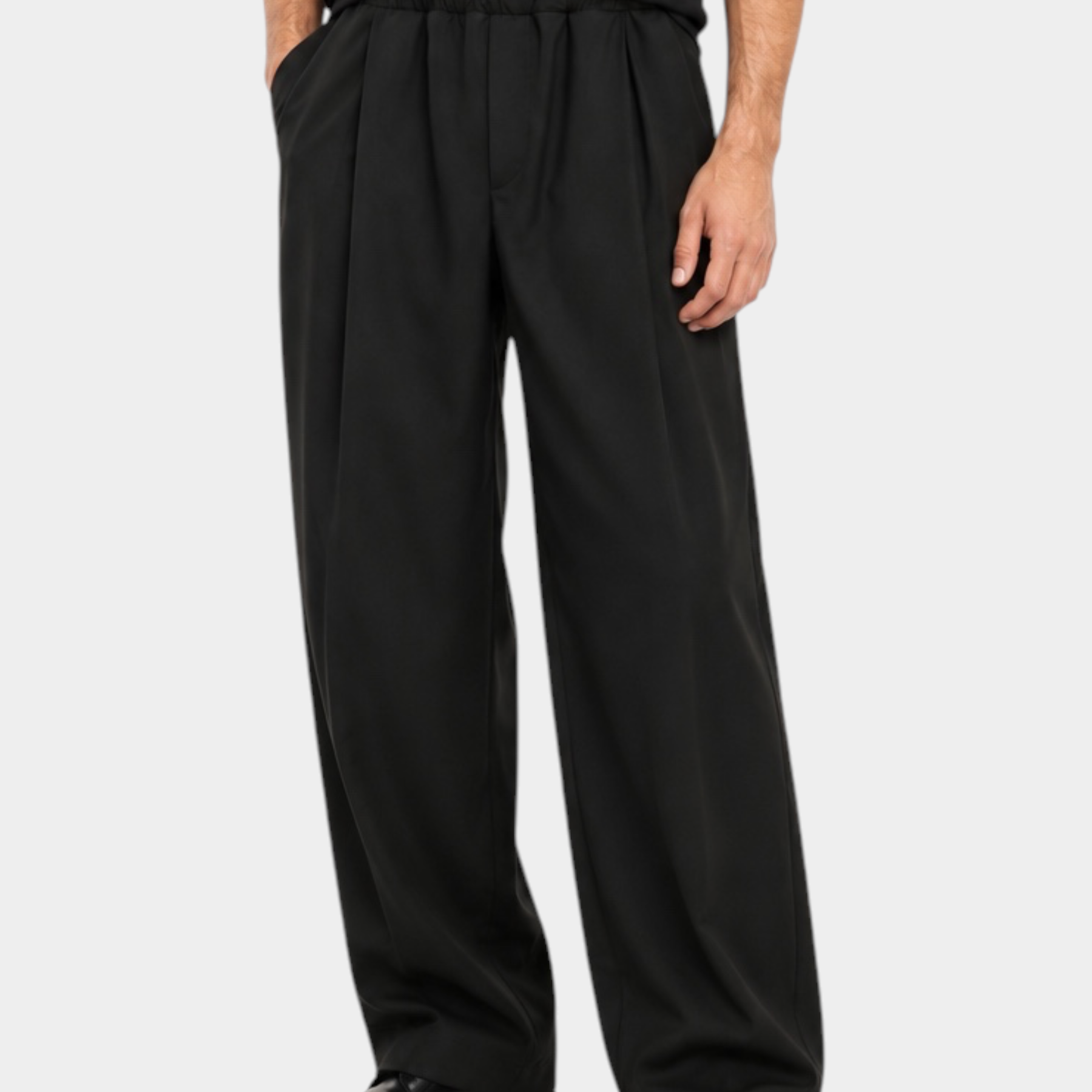 Modello indossa pantaloni baggy-fit con pinces Follower SRL in colore scuro con t-shirt nera e scarpe eleganti