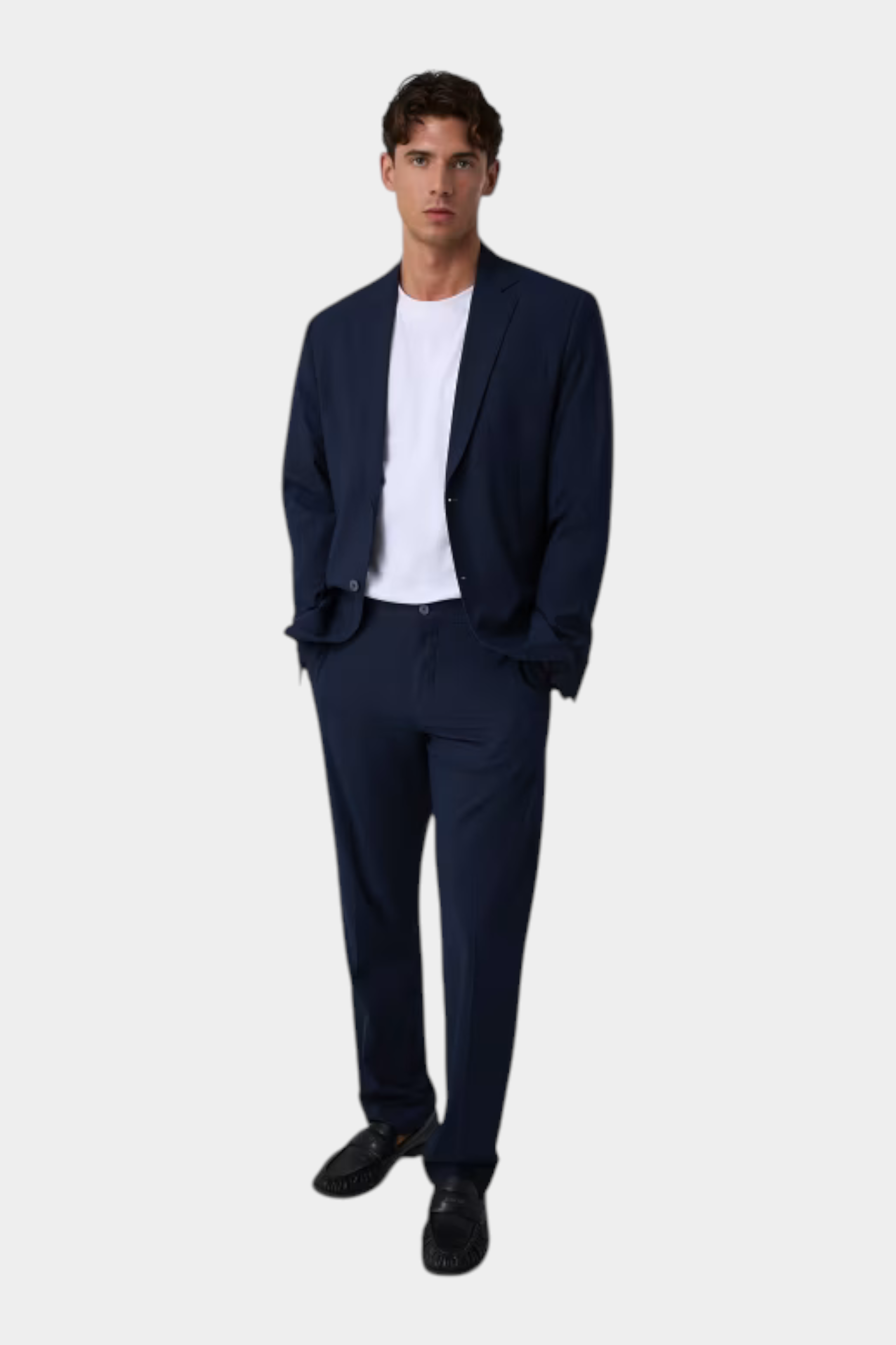 Modello indossa pantaloni classici blu GUESS con giacca abbinata e t-shirt bianca, collezione Follower SRL