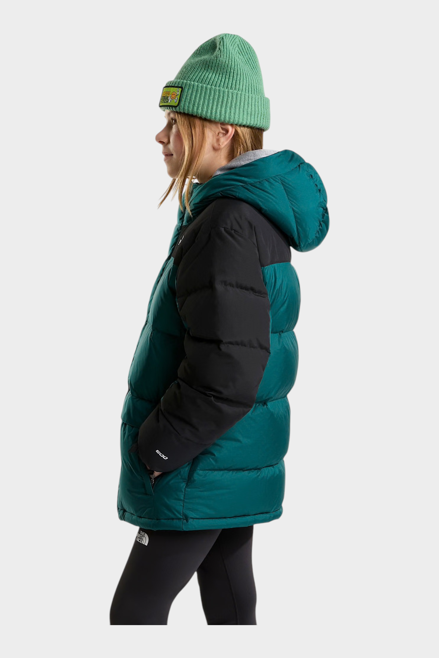 Modella di profilo indossa un parka corto Follower SRL The North Face verde e nero con cappuccio e berretto coordinato