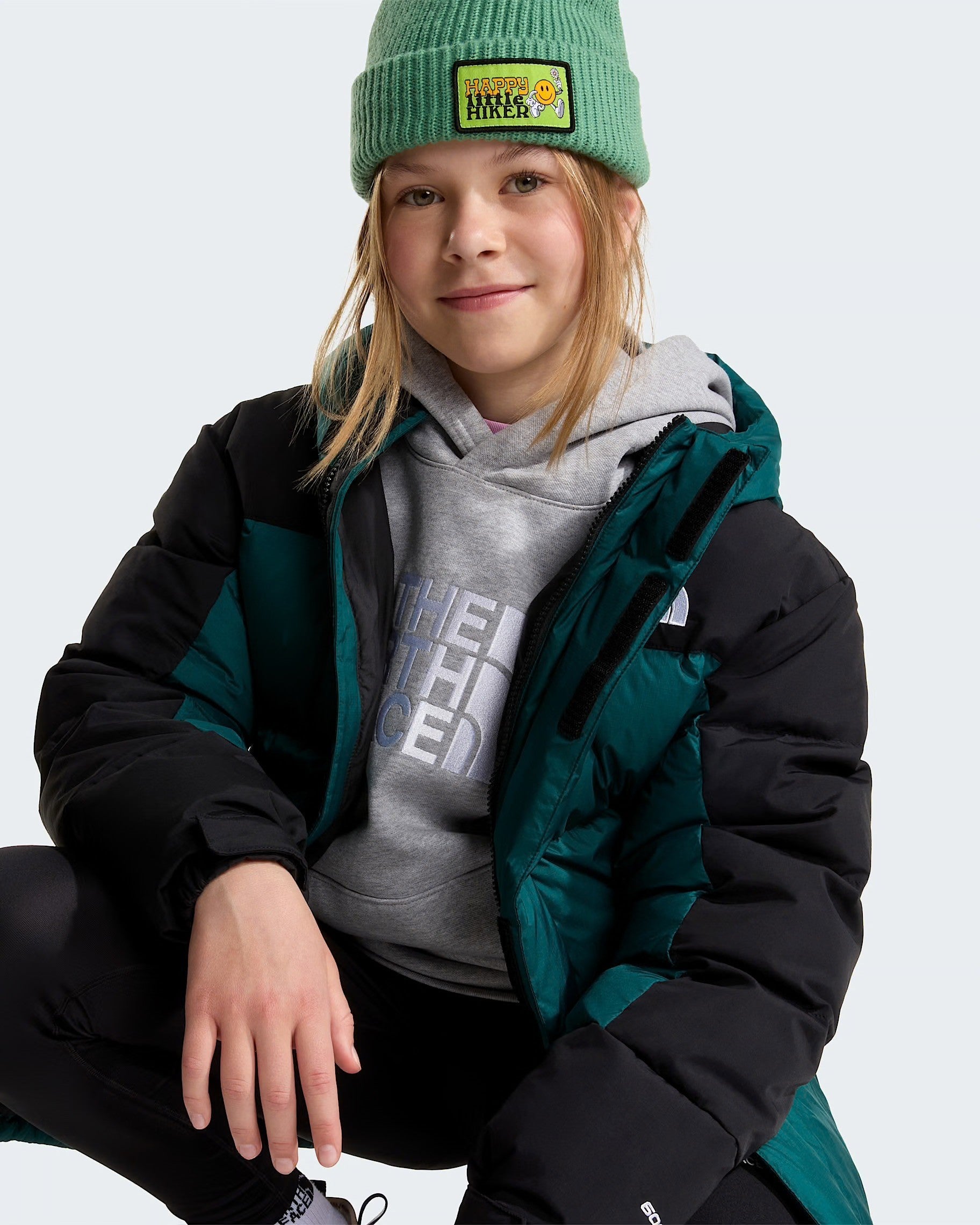 Ragazza indossa un parka corto Follower SRL The North Face verde e nero con imbottitura in piumino e berretto verde