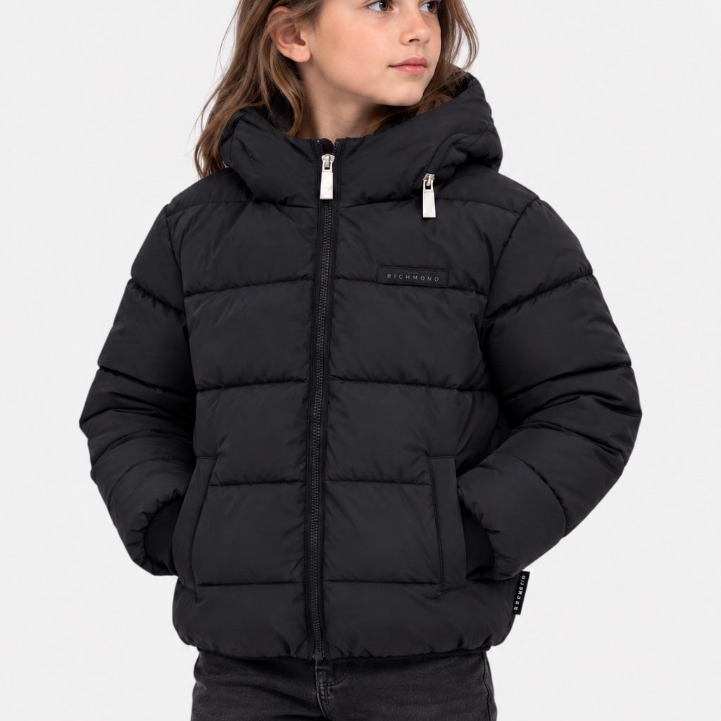 Bambina indossa piumino nero trapuntato Follower SRL con cappuccio, chiusura zip e logo Richmond sul petto.