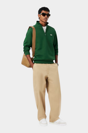 Modello Follower SRL indossa felpa verde con zip, pantaloni beige e sneakers in pelle bianche LACOSTE Slam Break