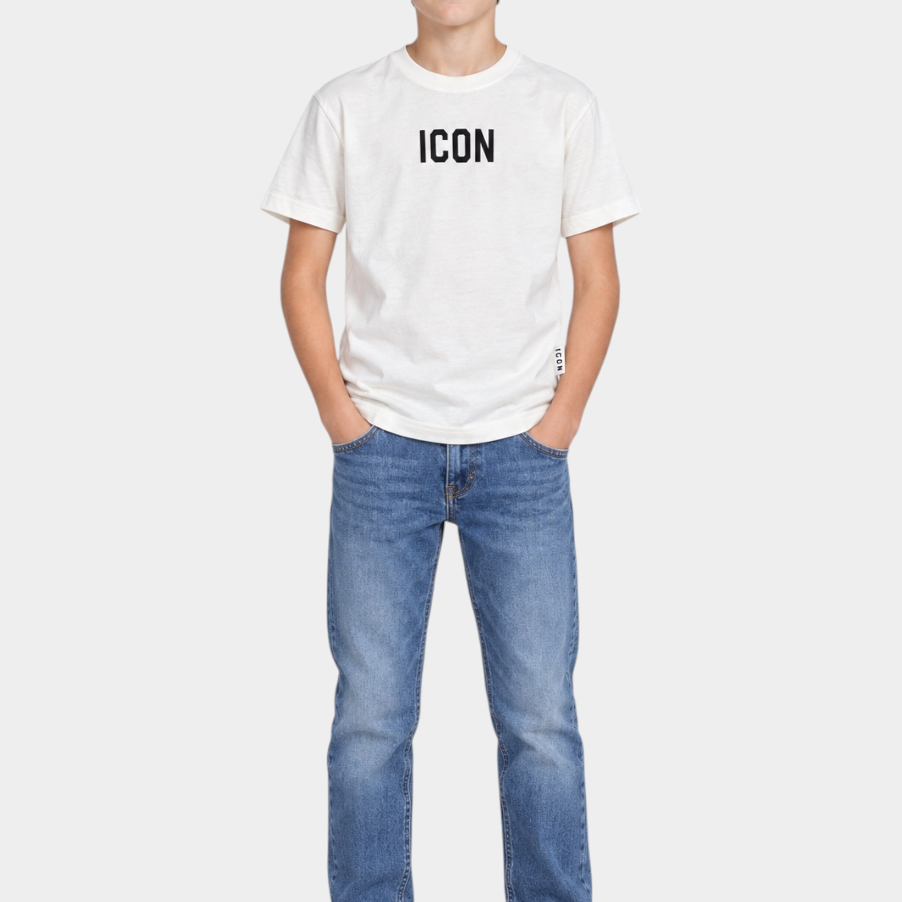 Ragazzo indossa t-shirt bianca Follower SRL con logo ICON nero, jeans blu e sneakers bianche su sfondo grigio
