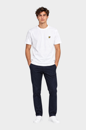 Modello indossa t-shirt bianca Follower SRL Lyle & Scott con logo dorato sul petto e pantaloni blu scuro