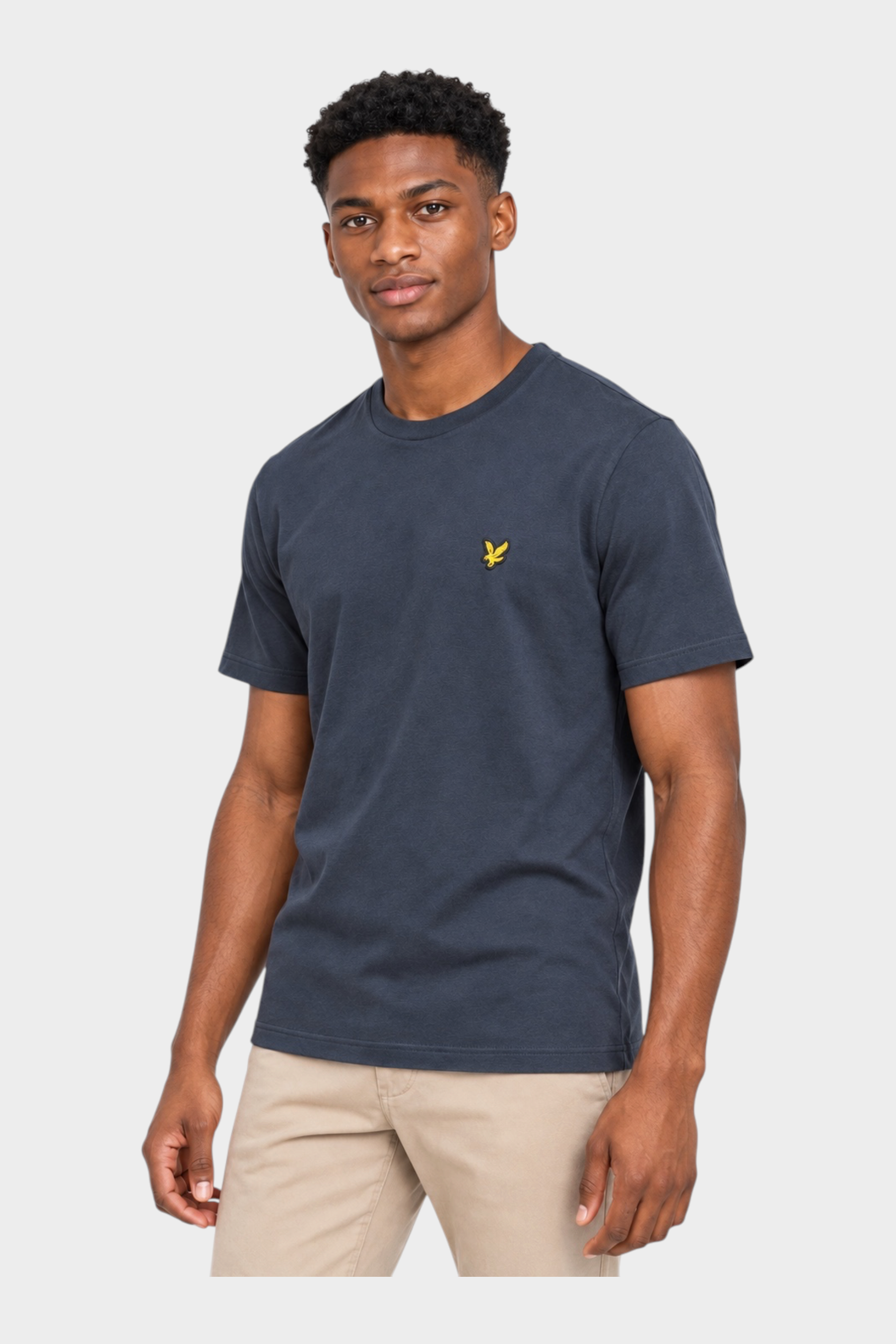 Modello indossa t-shirt blu Follower SRL con logo giallo Lyle & Scott sul petto e pantaloni beige