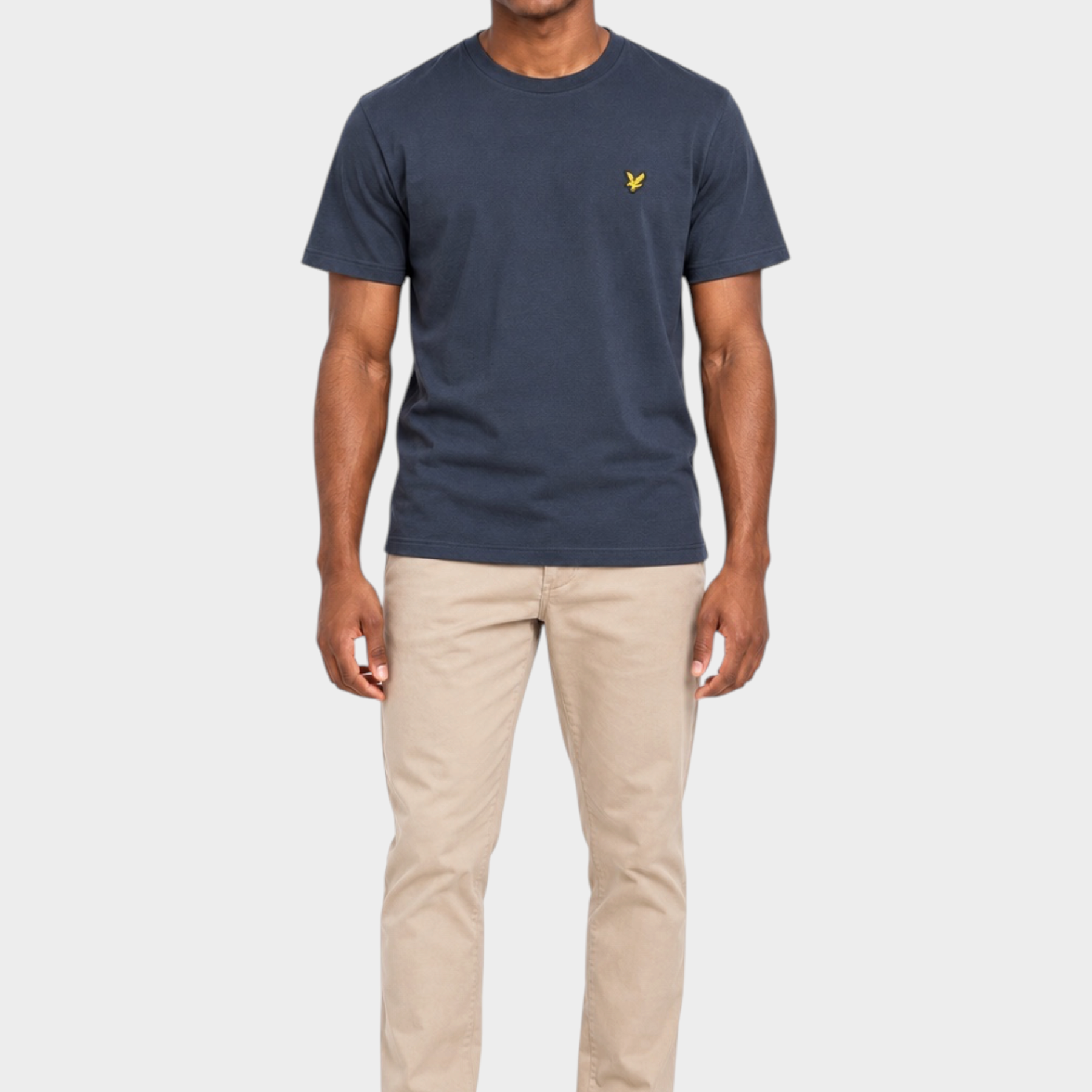 Modello indossa t-shirt blu scuro LYLE & SCOTT con logo giallo sul petto e pantaloni beige su sfondo bianco