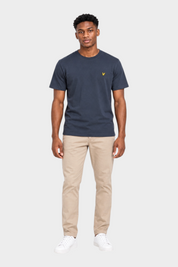 Modello indossa t-shirt blu scuro LYLE & SCOTT con logo giallo sul petto e pantaloni beige su sfondo bianco