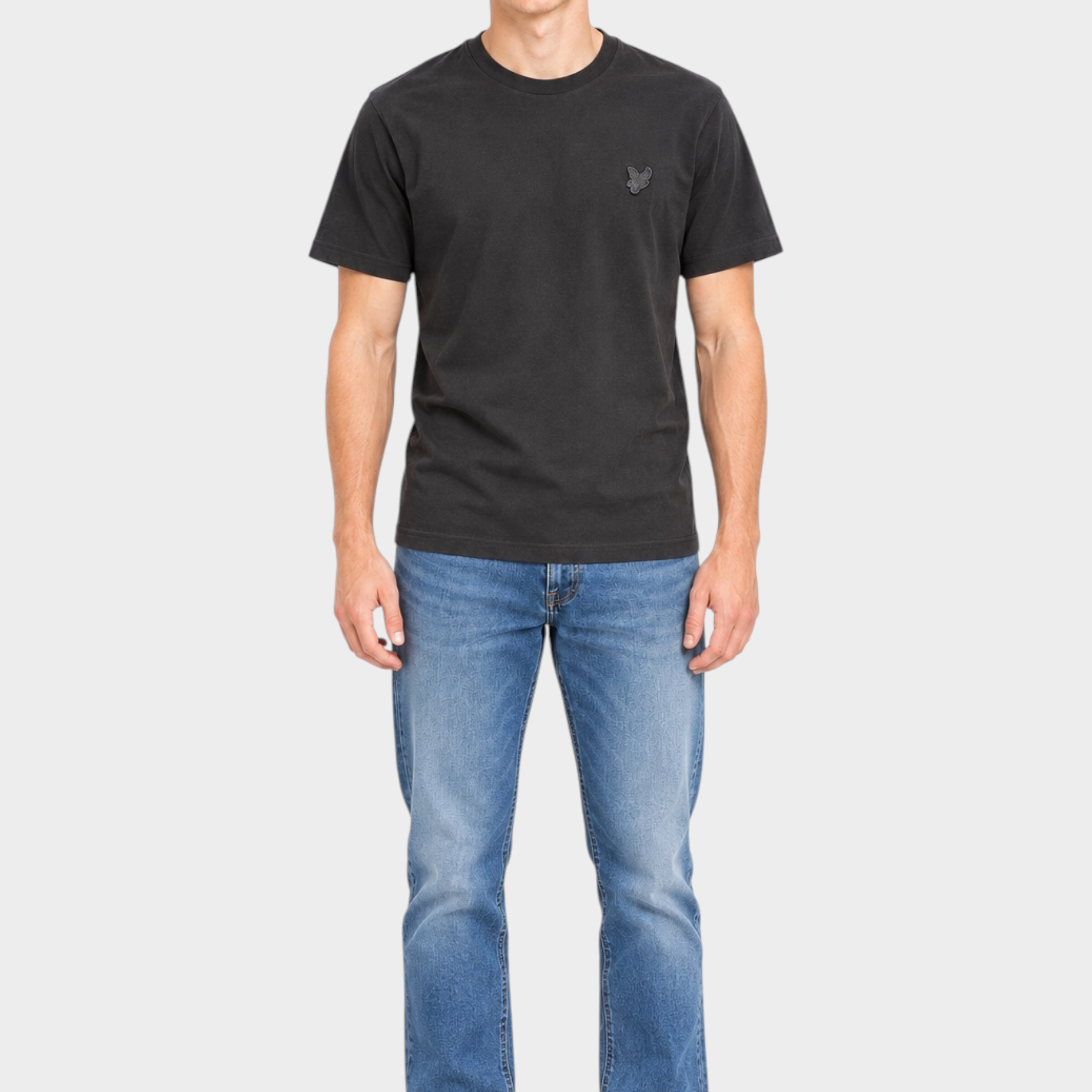 Modello indossa t-shirt nera Follower SRL Lyle & Scott con logo sul petto e jeans blu su sfondo neutro