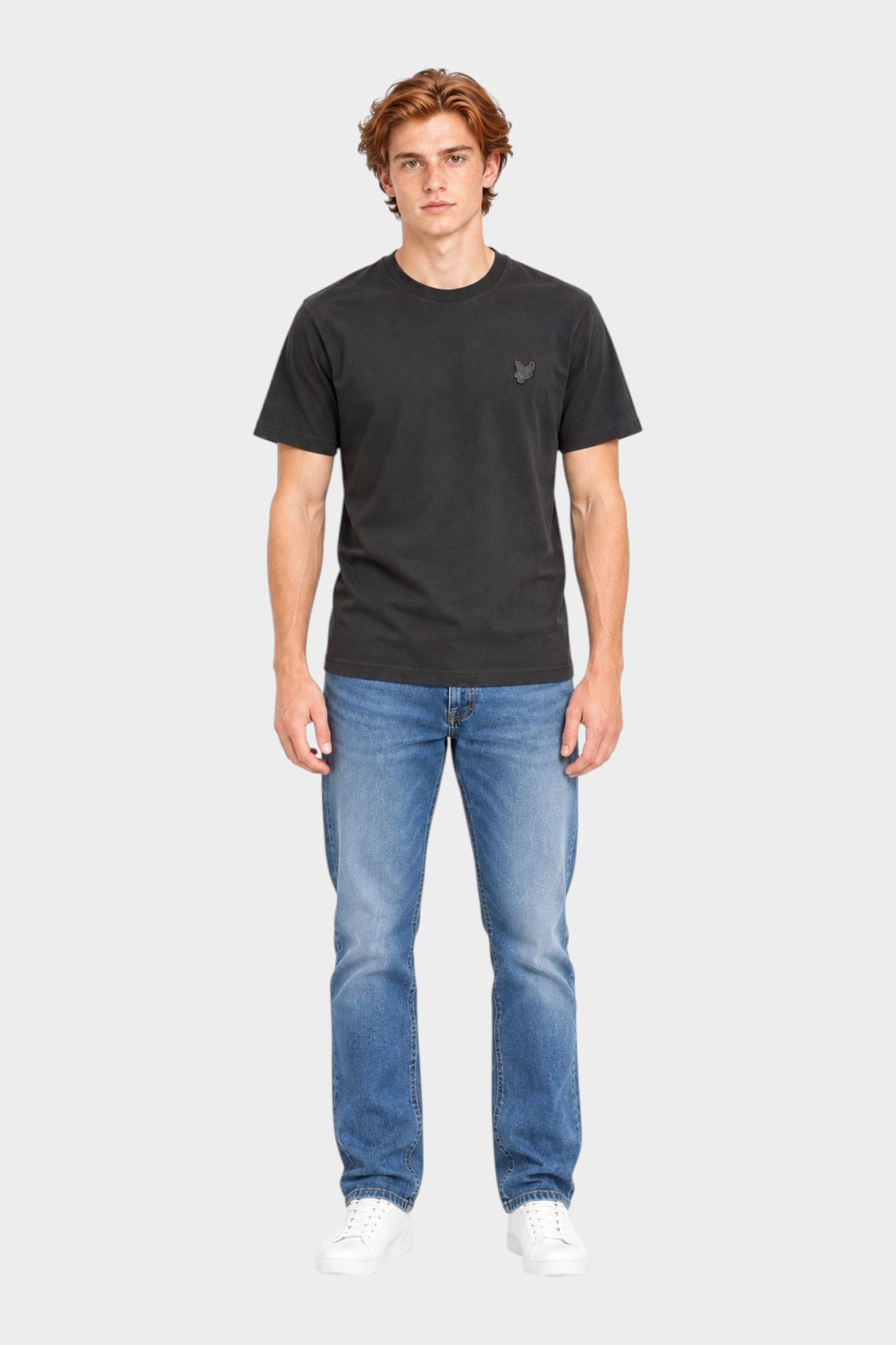 Modello indossa t-shirt nera Follower SRL Lyle & Scott con logo sul petto e jeans blu su sfondo neutro