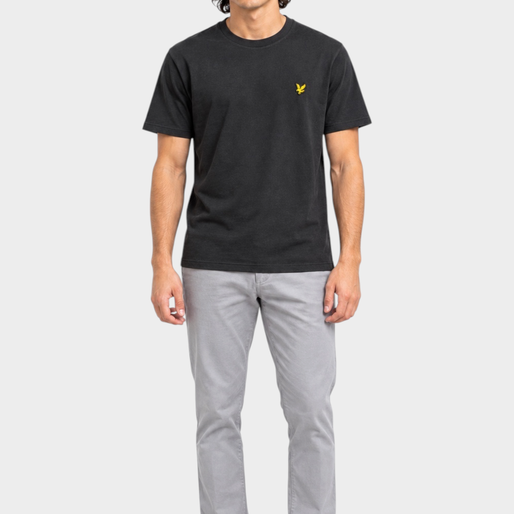 Modello indossa t-shirt nera Follower SRL Lyle & Scott con logo giallo sul petto e pantaloni grigi