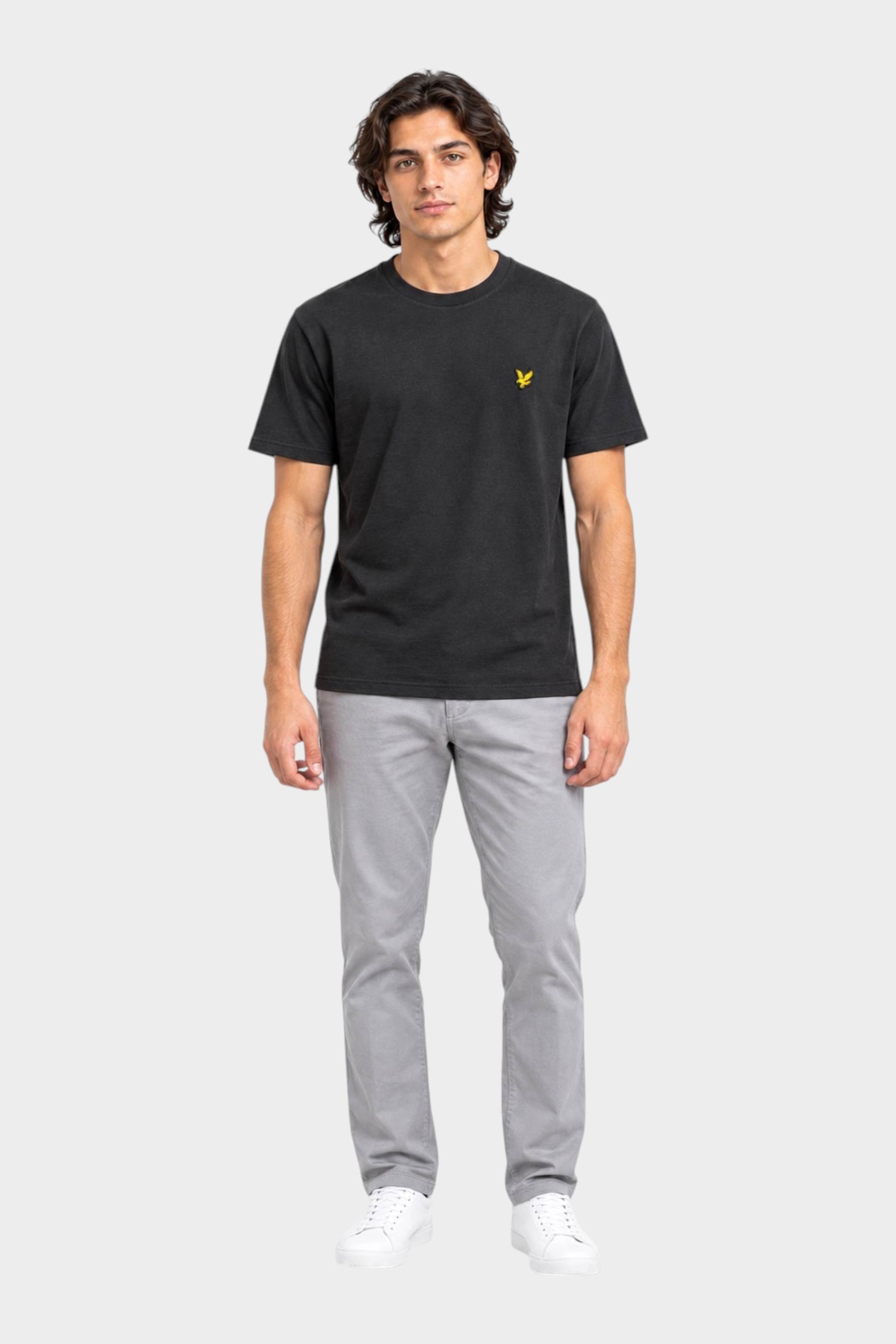 Modello indossa t-shirt nera Follower SRL Lyle & Scott con logo giallo sul petto e pantaloni grigi