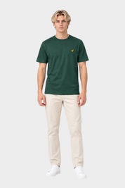 Modello indossa t-shirt verde Follower SRL con logo giallo sul petto, abbinata a pantaloni beige e scarpe bianche